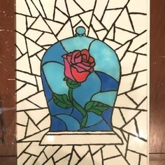 a stained glass window with a red rose in a blue vase on it's side