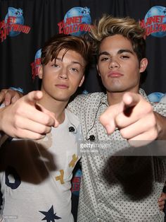 two young men pointing their fingers at the camera in front of a black backdrop with red and