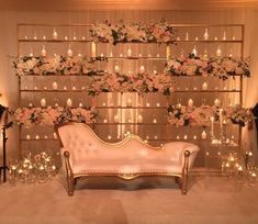 a white couch sitting in front of a wall with candles and flowers on top of it