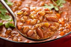 a spoon full of chili and beans with cilantro leaves on the side in a red pot