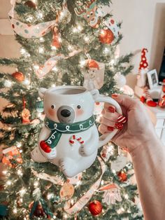 a person holding a coffee mug in front of a christmas tree with ornaments on it