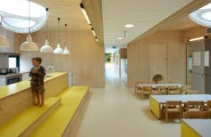 a young boy standing at the end of a yellow counter in a room filled with tables and chairs