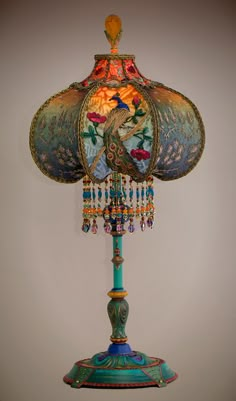 an ornate lamp is on display against a white wall with a blue base and colorful beaded lampshade