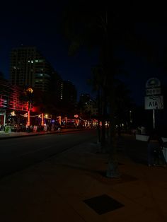 the city street is lit up at night with bright lights and palm trees in the foreground