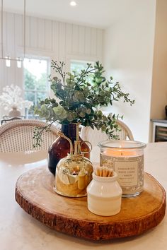 a candle and some flowers on a wooden tray in front of a dining room table