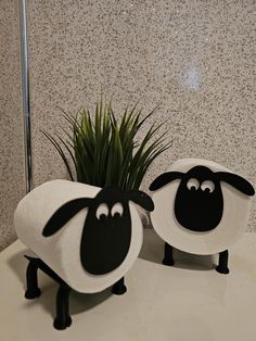 two black and white sheep sitting on top of a counter next to a potted plant