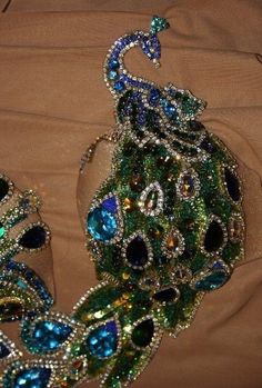 a peacock made out of beads and jewels on top of a brown cloth covered bed