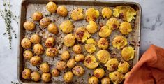 a baking pan filled with potatoes on top of a marble counter next to an orange napkin