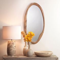 a vase with flowers on a table next to a mirror and lamp in a room