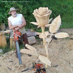 a man standing next to a large wooden rose with a chainsaw on the ground