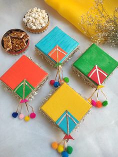 four small colorful squares with pom - poms on them next to a bowl of popcorn