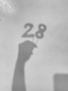 the shadow of a person holding a small object in their hand with the number 28 on it