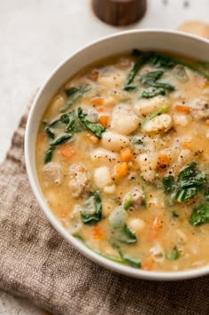 a white bowl filled with soup on top of a cloth next to a wooden spoon