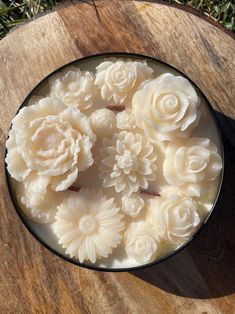 a bowl filled with white frosted flowers on top of a wooden table next to grass