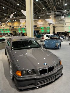 several cars are on display in a showroom with people looking at them from the front