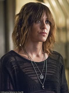 a woman with brown hair wearing a black shirt and silver necklace, looking off to the side