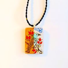 a necklace with a bird painted on the front and back of it, hanging from a black cord