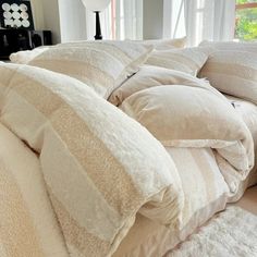 an unmade bed with several pillows on top of it in front of a window