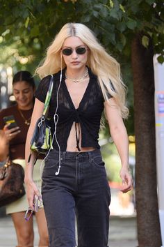 a woman with long blonde hair walking down the street wearing headphones and carrying a purse