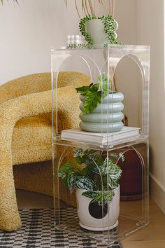 a clear shelf with plants on top of it next to a yellow chair and black and white checkered rug