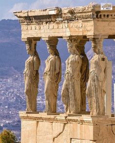 some statues on the side of a building with a city in the backgroud