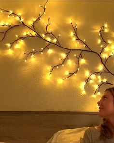 a woman sitting in bed looking up at a tree with lights on it