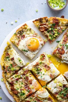 an egg and cheese pizza cut into squares on a white plate next to a bowl of green onions