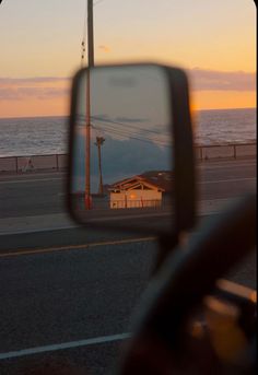 a side view mirror on the back of a car next to an ocean at sunset