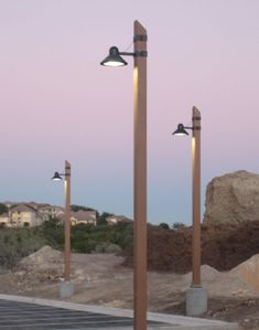 three street lamps are standing in the middle of a road with rocks and dirt behind them