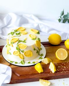 a cake with lemons and leaves on it sitting on a cutting board next to sliced lemons