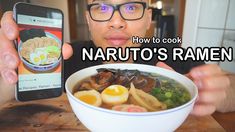 a man is holding up his cell phone while he eats ramen