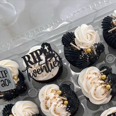 cupcakes decorated with white frosting and black icing in a plastic container