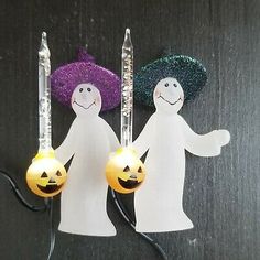 two white plastic figures holding pumpkins and lights