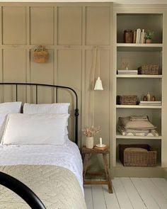 a white bed sitting in a bedroom next to a wooden shelf filled with books and other items