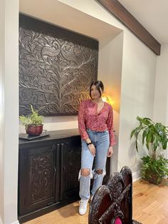 a woman standing next to a bed in a room with wooden floors and walls, wearing ripped jeans