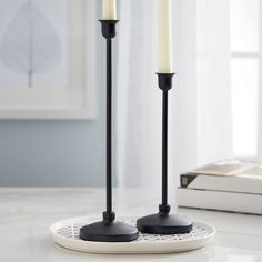 two black candles are sitting on a white plate with a book in the back ground