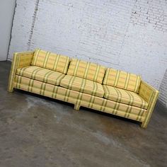 a yellow plaid couch sitting in front of a white brick wall on concrete flooring