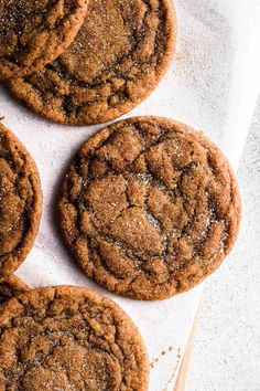 four chocolate cookies with sugar on top sitting on a piece of parchment paper next to a wooden spoon