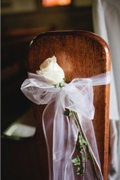 a single white rose tied to the back of a wooden chair at a wedding ceremony