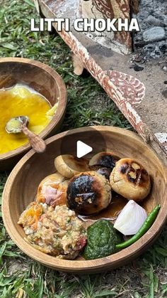 two wooden bowls filled with food sitting on top of a grass covered field next to an open fire