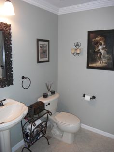 a white toilet sitting next to a sink in a bathroom under a painting on the wall