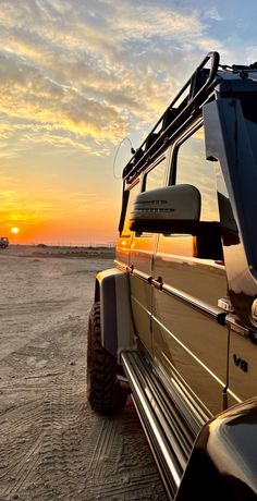 an suv parked on the beach at sunset