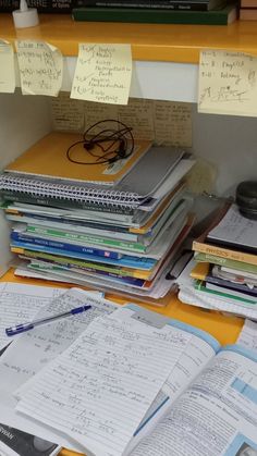 many books and papers are stacked on top of each other in front of a desk