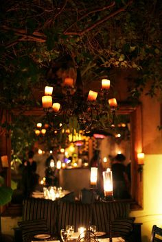 an outdoor dining area with lit candles and tables in the center, surrounded by greenery