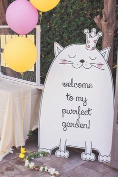 a welcome sign with balloons in the shape of a cat and a crown on top