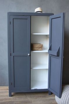 an armoire with two doors and shelves on the inside, in front of a gray wall