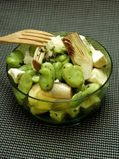 a glass bowl filled with green vegetables on top of a black table cloth next to a wooden utensil