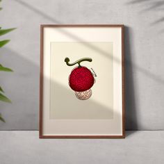 a framed art print with a red apple on it's side next to a potted plant