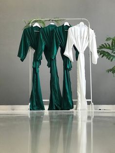 three green and white robes hanging on a rack next to a potted plant in a room