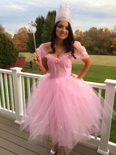 a woman in a pink dress is standing on a porch holding a wand and wearing a tiara